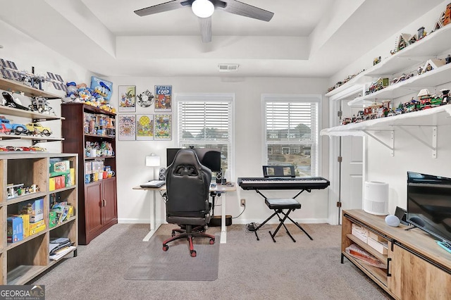 carpeted home office with ceiling fan and a tray ceiling