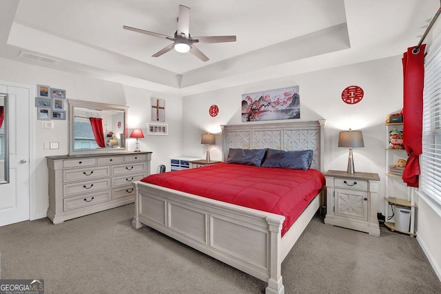 bedroom with ceiling fan, a tray ceiling, and light carpet