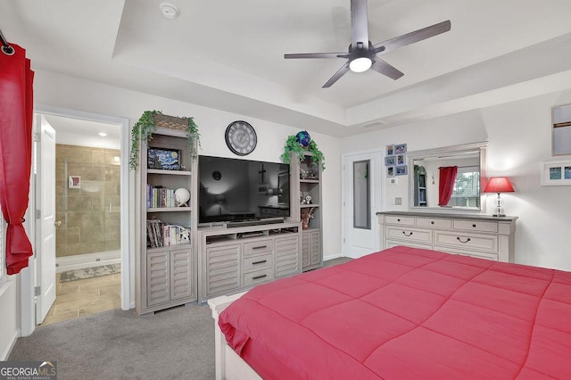 carpeted bedroom with a raised ceiling, ceiling fan, and ensuite bath