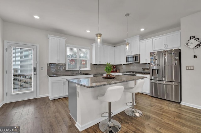 kitchen featuring appliances with stainless steel finishes, decorative light fixtures, white cabinetry, sink, and a center island