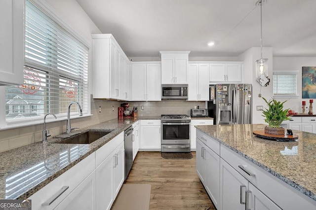 kitchen with stainless steel appliances, hanging light fixtures, sink, and white cabinets