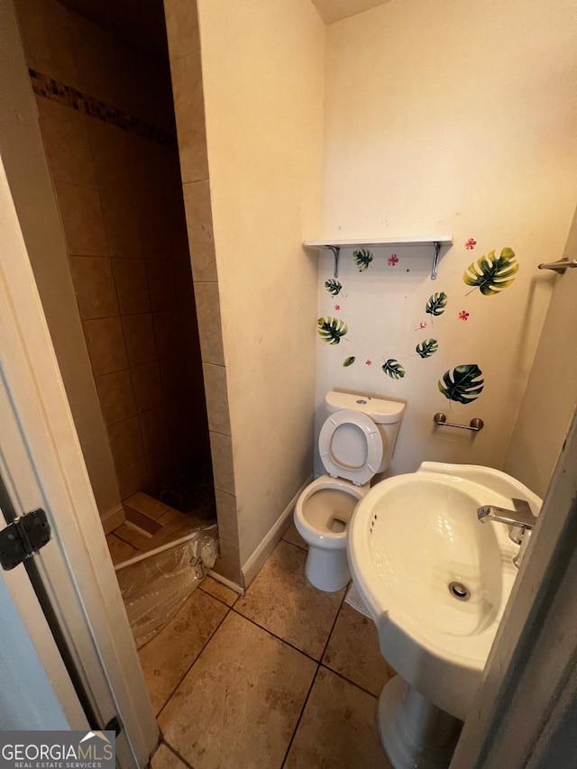 bathroom with tile patterned flooring, sink, a tile shower, and toilet