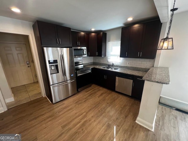 kitchen featuring pendant lighting, sink, stainless steel appliances, light stone countertops, and light hardwood / wood-style flooring