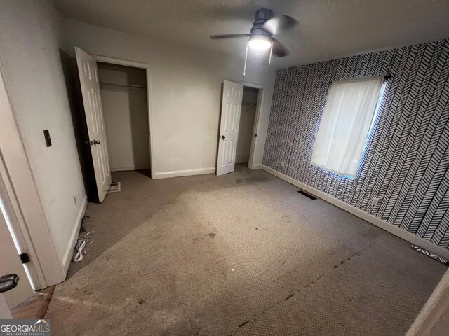 unfurnished bedroom featuring ceiling fan, carpet floors, and multiple closets