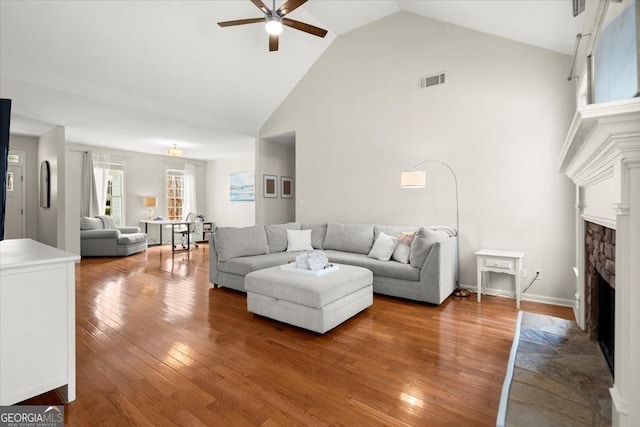 living room featuring hardwood / wood-style floors, a stone fireplace, high vaulted ceiling, and ceiling fan