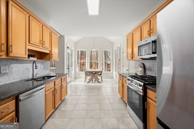 kitchen with decorative light fixtures, lofted ceiling, sink, dark stone counters, and stainless steel appliances