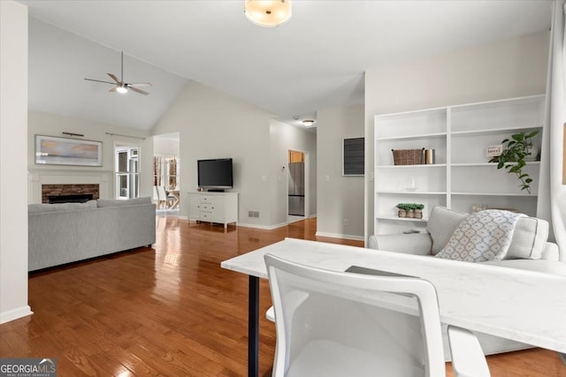 living room featuring ceiling fan, wood-type flooring, a fireplace, and vaulted ceiling