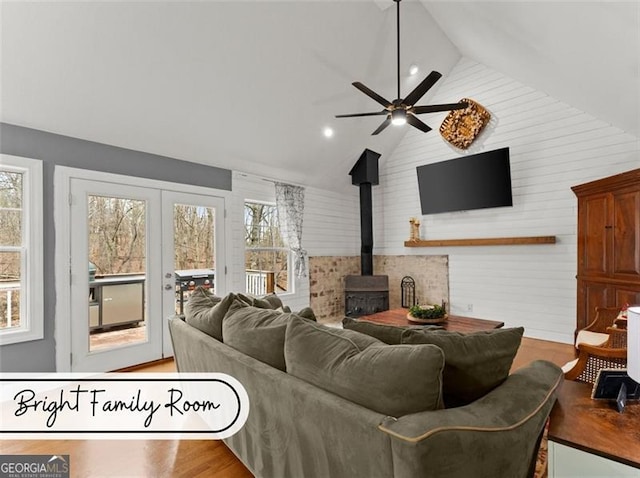 living room featuring high vaulted ceiling, wood-type flooring, a wood stove, ceiling fan, and french doors