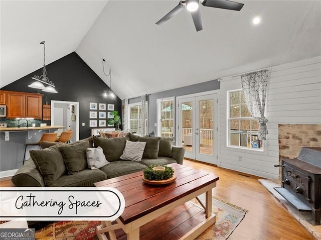 living room featuring high vaulted ceiling, a wood stove, ceiling fan, light hardwood / wood-style floors, and french doors