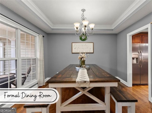 dining area featuring an inviting chandelier, ornamental molding, a tray ceiling, and hardwood / wood-style floors