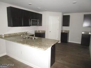 kitchen featuring light stone countertops, dark wood-type flooring, sink, and kitchen peninsula