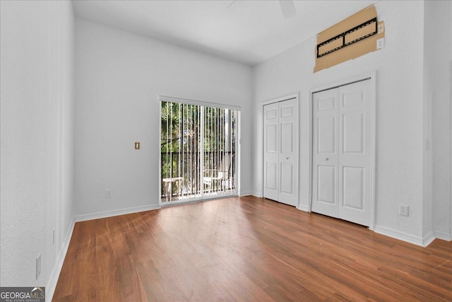 unfurnished bedroom with access to exterior, hardwood / wood-style flooring, multiple closets, and ceiling fan