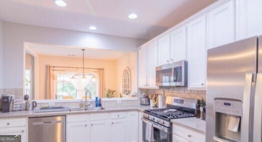 kitchen featuring pendant lighting, sink, appliances with stainless steel finishes, white cabinetry, and tasteful backsplash