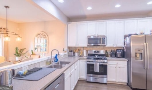 kitchen with sink, hanging light fixtures, stainless steel appliances, white cabinets, and kitchen peninsula