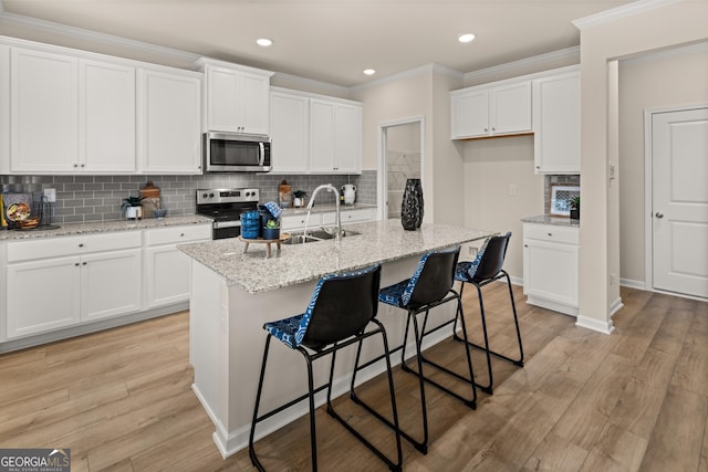 kitchen with sink, stainless steel appliances, light stone counters, an island with sink, and white cabinets