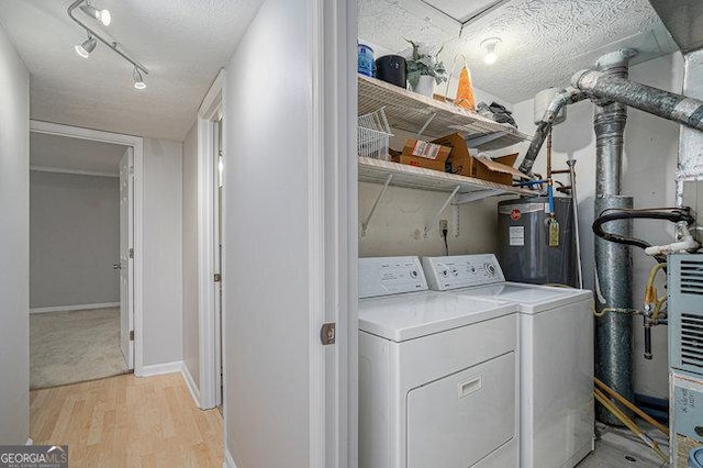 clothes washing area with washing machine and clothes dryer, electric water heater, a textured ceiling, and light wood-type flooring