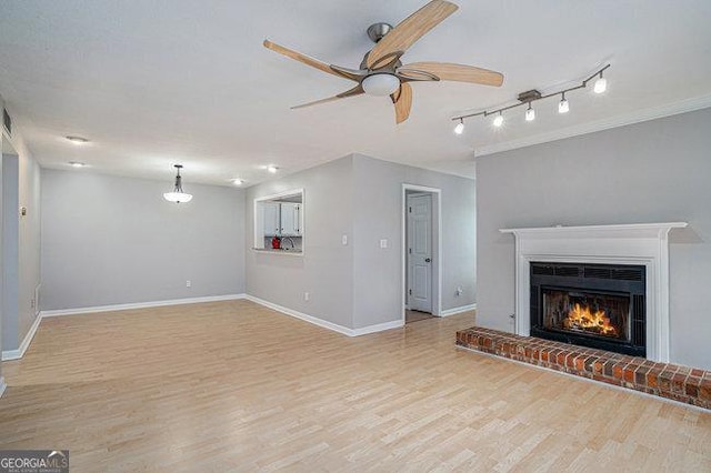 unfurnished living room featuring ceiling fan, a brick fireplace, track lighting, and light wood-type flooring