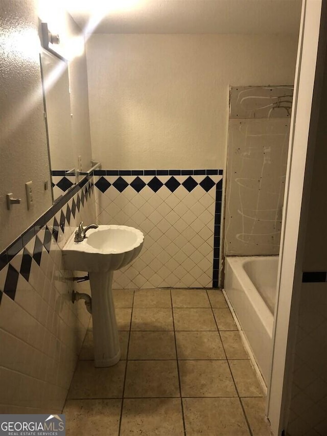 bathroom featuring a tub to relax in, sink, tile patterned flooring, and tile walls