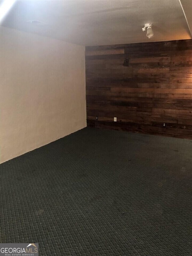 basement featuring dark carpet and wood walls