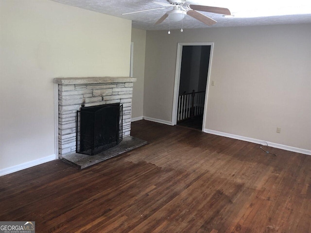 unfurnished living room featuring dark wood-type flooring, ceiling fan, and a stone fireplace