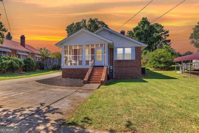 bungalow-style home with a carport, a yard, and a sunroom