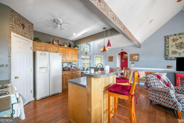 kitchen with white appliances, a kitchen island with sink, a kitchen breakfast bar, lofted ceiling with beams, and light brown cabinetry