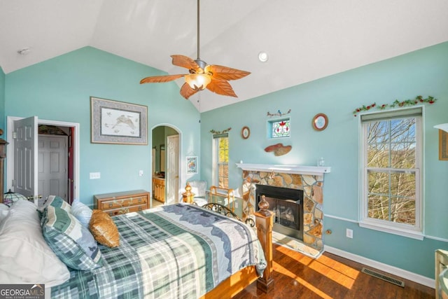 bedroom featuring lofted ceiling, hardwood / wood-style floors, a stone fireplace, and ceiling fan