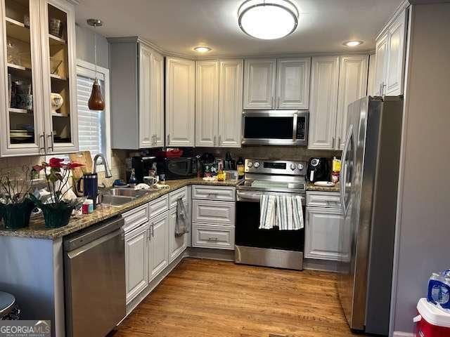 kitchen featuring stainless steel appliances, white cabinetry, light wood-type flooring, and dark stone counters