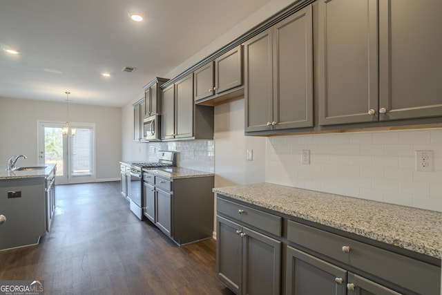 kitchen with appliances with stainless steel finishes, dark hardwood / wood-style floors, decorative light fixtures, sink, and light stone counters