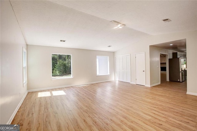 empty room with lofted ceiling, a textured ceiling, and light wood-type flooring