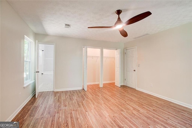 unfurnished bedroom featuring ensuite bathroom, light hardwood / wood-style flooring, a textured ceiling, multiple closets, and ceiling fan