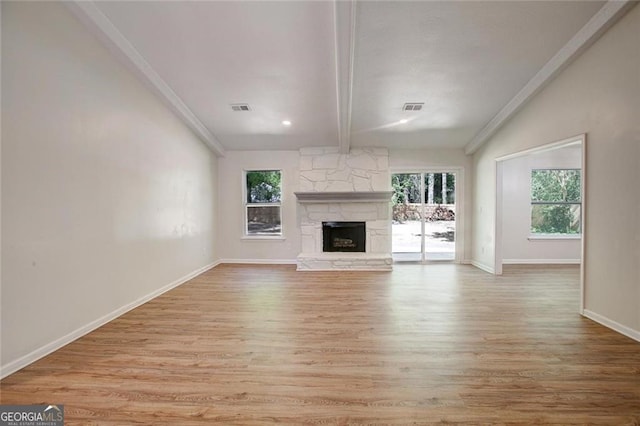 unfurnished living room with lofted ceiling with beams, a stone fireplace, a wealth of natural light, and light hardwood / wood-style floors