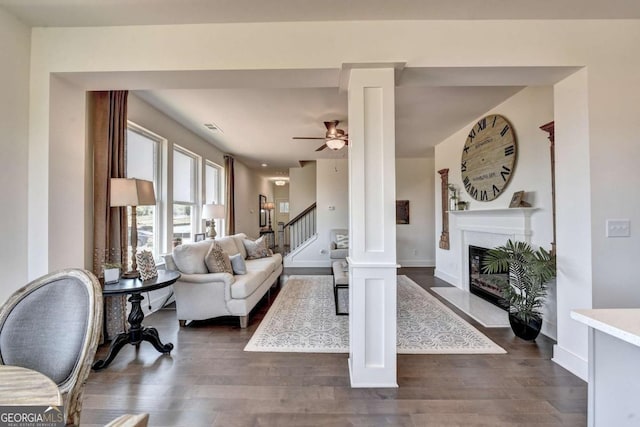 living room featuring dark wood-type flooring, ceiling fan, and ornate columns