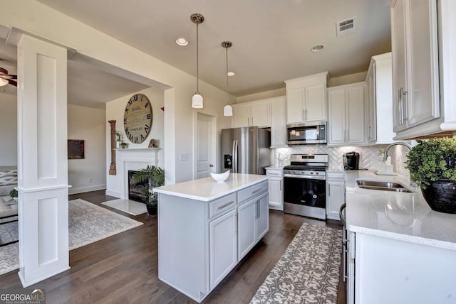 kitchen with sink, decorative light fixtures, appliances with stainless steel finishes, a kitchen island, and white cabinets