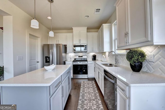 kitchen with sink, appliances with stainless steel finishes, a center island, white cabinets, and decorative light fixtures