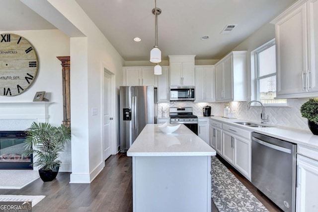 kitchen with a kitchen island, appliances with stainless steel finishes, decorative light fixtures, sink, and white cabinets