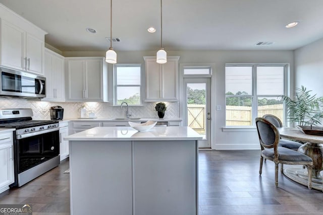 kitchen featuring white cabinetry, stainless steel appliances, decorative light fixtures, and a kitchen island