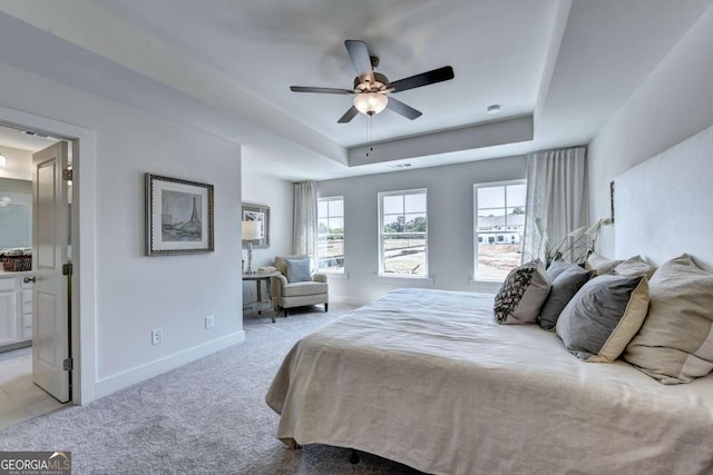 bedroom featuring ceiling fan, ensuite bathroom, a raised ceiling, and light carpet