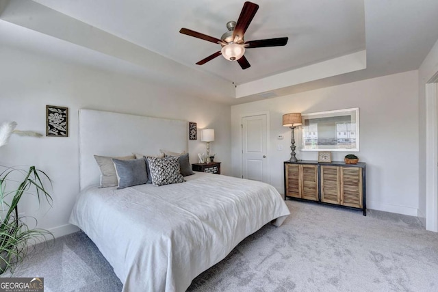 carpeted bedroom featuring a tray ceiling and ceiling fan