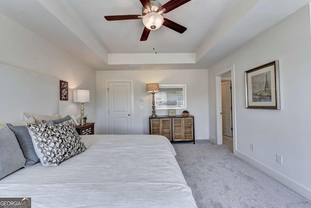 bedroom featuring a tray ceiling, light colored carpet, and ceiling fan