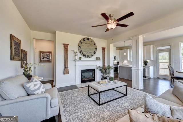 living room featuring dark wood-type flooring, ceiling fan, and ornate columns