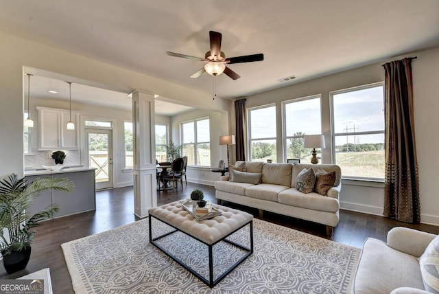 living room featuring decorative columns, ceiling fan, a healthy amount of sunlight, and dark hardwood / wood-style flooring