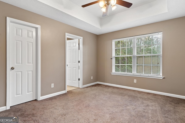 unfurnished bedroom featuring light carpet, a tray ceiling, and ceiling fan