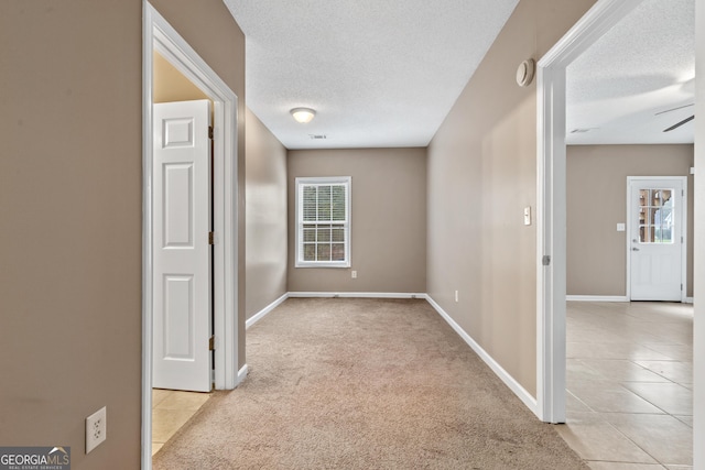 hall with light colored carpet and a textured ceiling