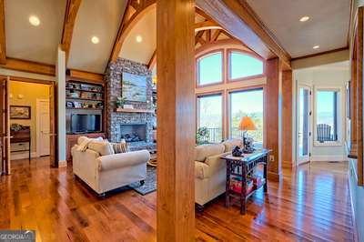 living room with built in shelves, wood-type flooring, a stone fireplace, and lofted ceiling with beams