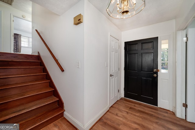 entryway with baseboards, stairs, an inviting chandelier, wood finished floors, and a textured ceiling