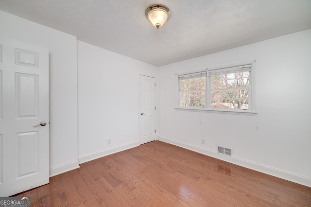 unfurnished room with a textured ceiling, wood finished floors, visible vents, and baseboards