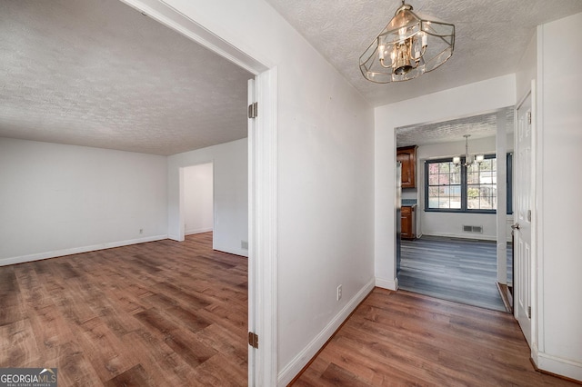 corridor featuring visible vents, baseboards, an inviting chandelier, and wood finished floors