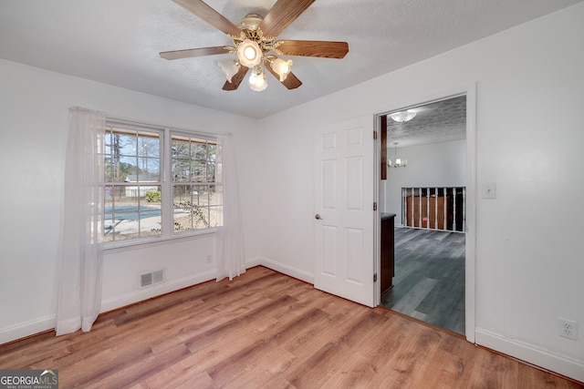 unfurnished room featuring light wood finished floors, visible vents, a textured ceiling, and a ceiling fan