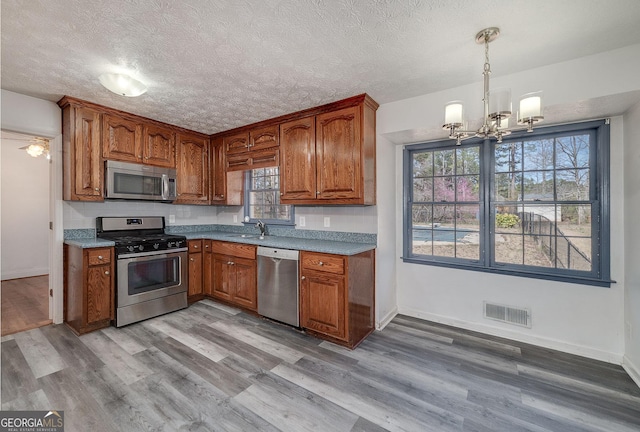 kitchen with brown cabinets, visible vents, a chandelier, and stainless steel appliances